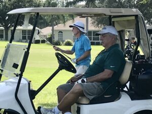 golfers on the course, one in the golf cart and the other getting ready to hit his ball.